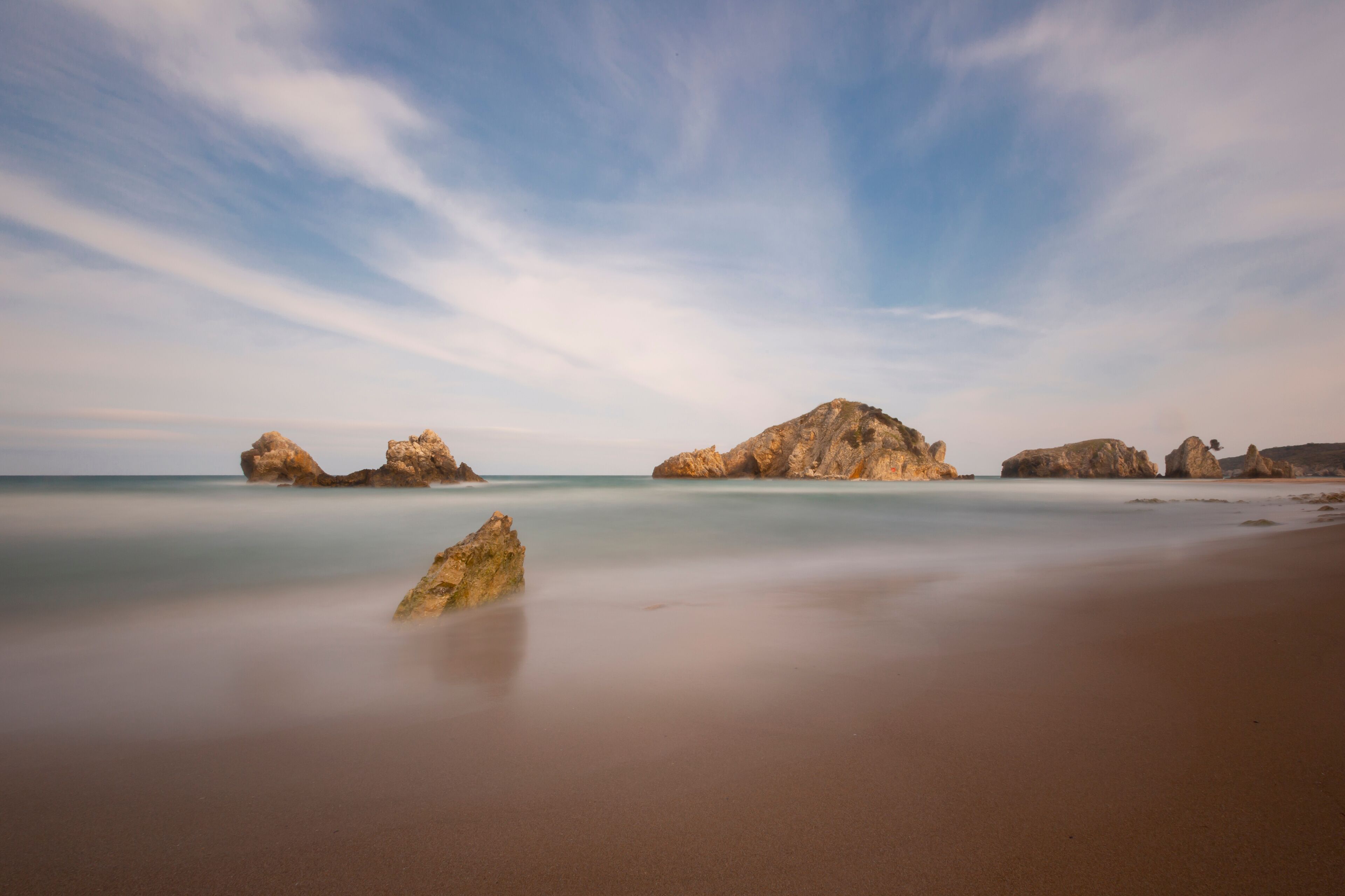 A beach with smooth water and large rock formations.