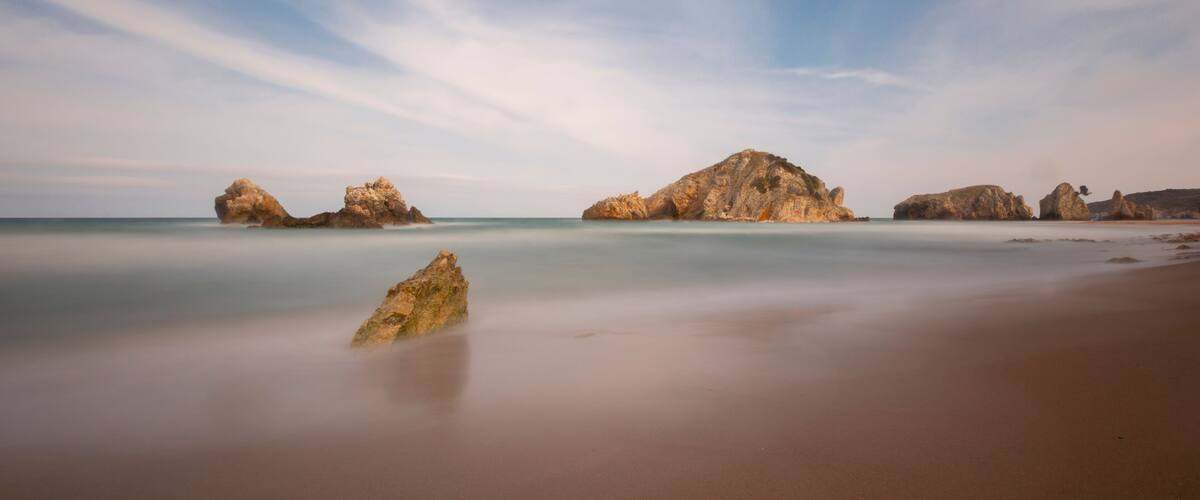 A beach with smooth water and large rock formations.