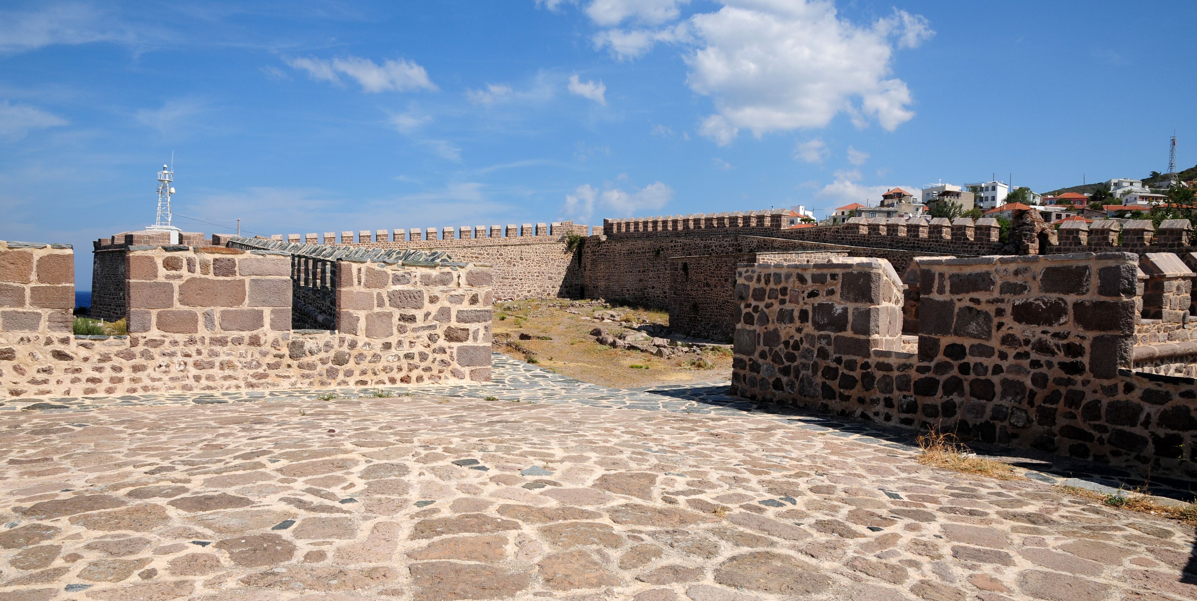 A stone fortification with a watchtower, cobblestone pathways, and a clear blue sky.