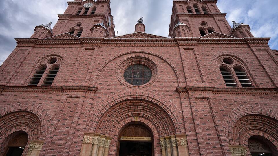 A large brick church with two towers, a large circular window, and an arched entrance.