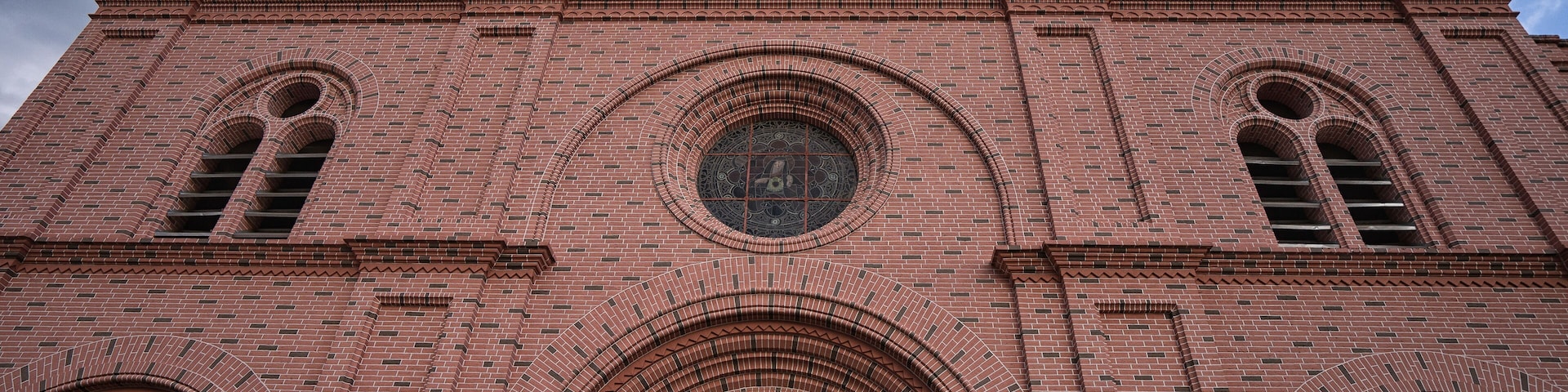 A large brick church with two towers, a large circular window, and an arched entrance.