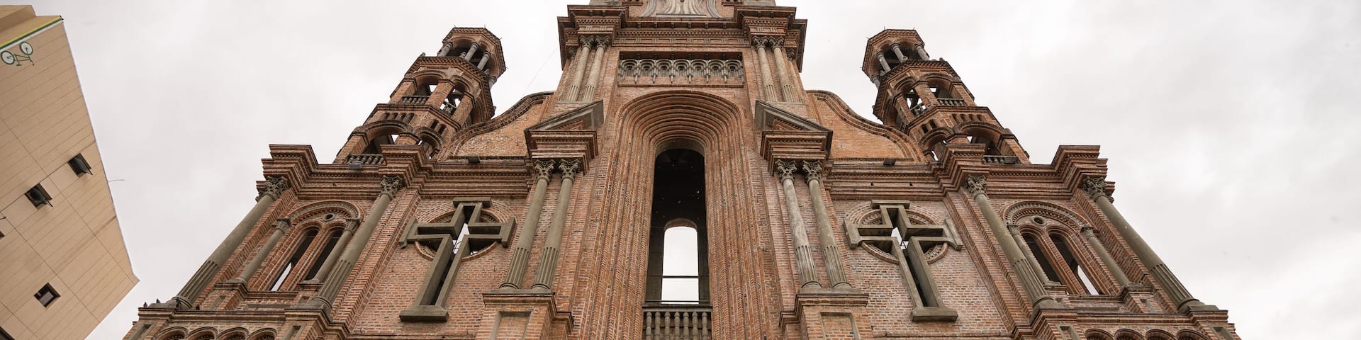 A large brick church with a central arched doorway, two bell towers, and a clock at the top.