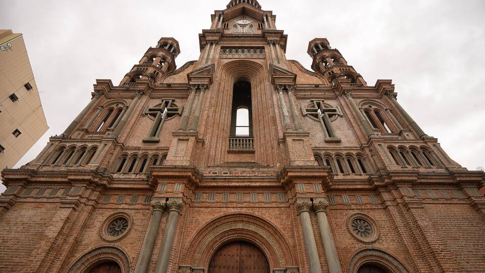 A large brick church with a central arched doorway, two bell towers, and a clock at the top.