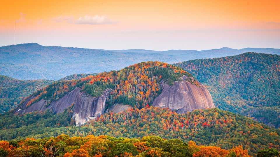 A mountainous landscape with a prominent rock formation and dense autumn foliage.