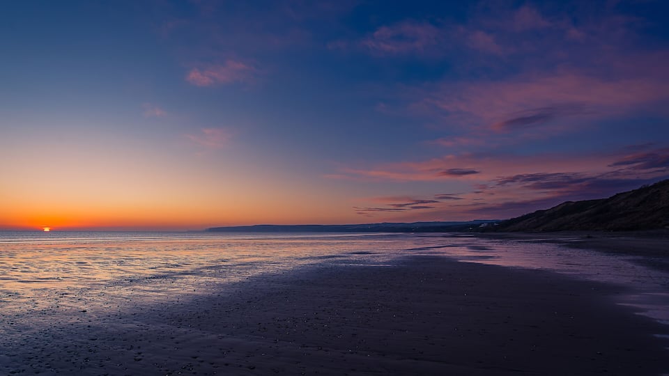 A sunset over a beach with calm waters reflecting the sky.