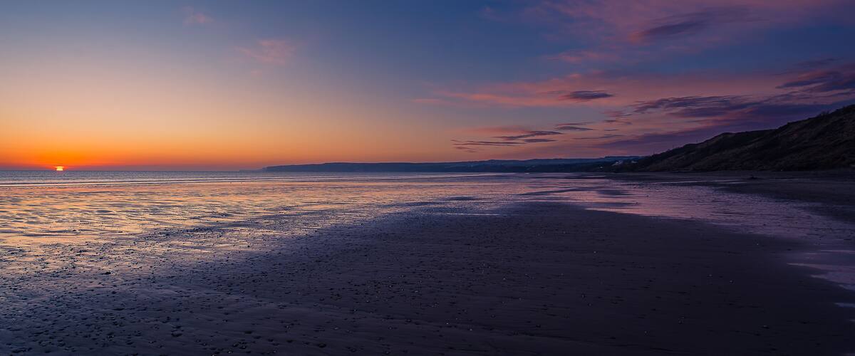 A sunset over a beach with calm waters reflecting the sky.