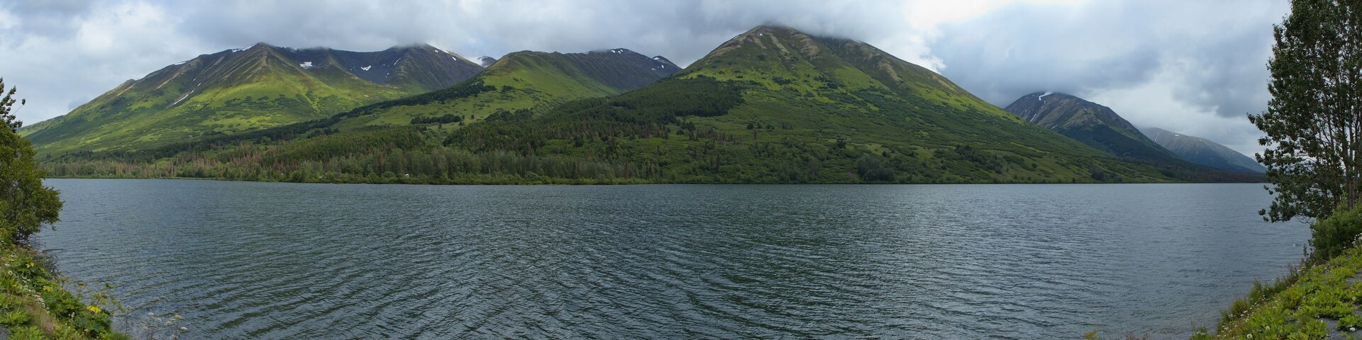 Un lago rodeado de montañas con parches de nieve.