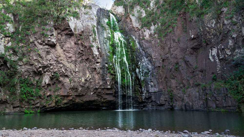 Ein Wasserfall stürzt über eine felsige Klippe in einen ruhigen Fluss.