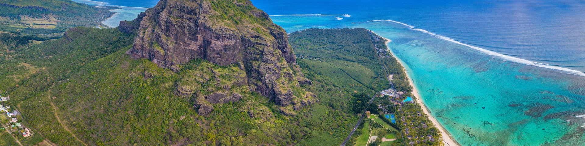 A mountainous landscape with a coastal area featuring clear turquoise waters and a small settlement.