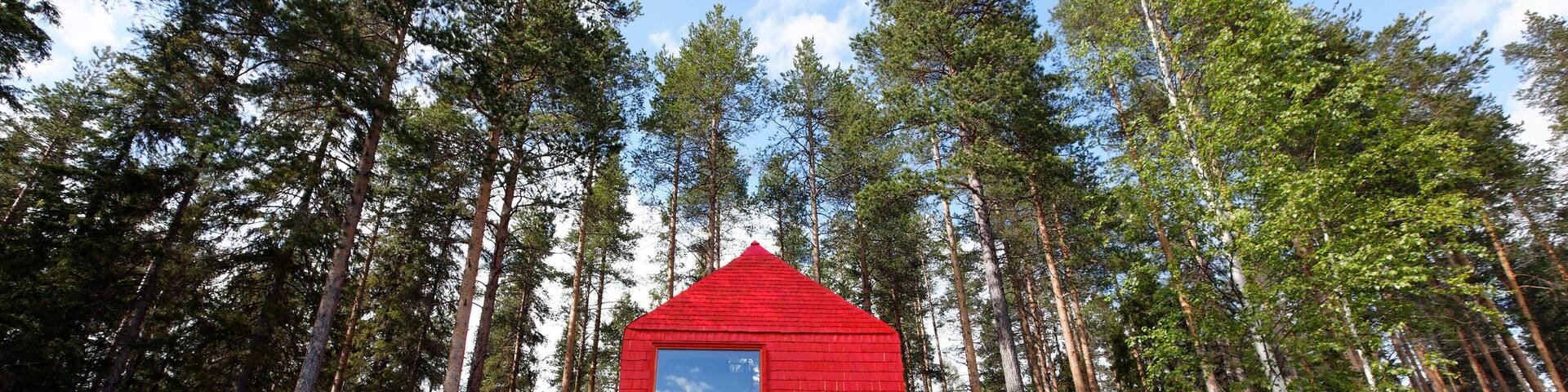 A red wooden cabin in a forest.