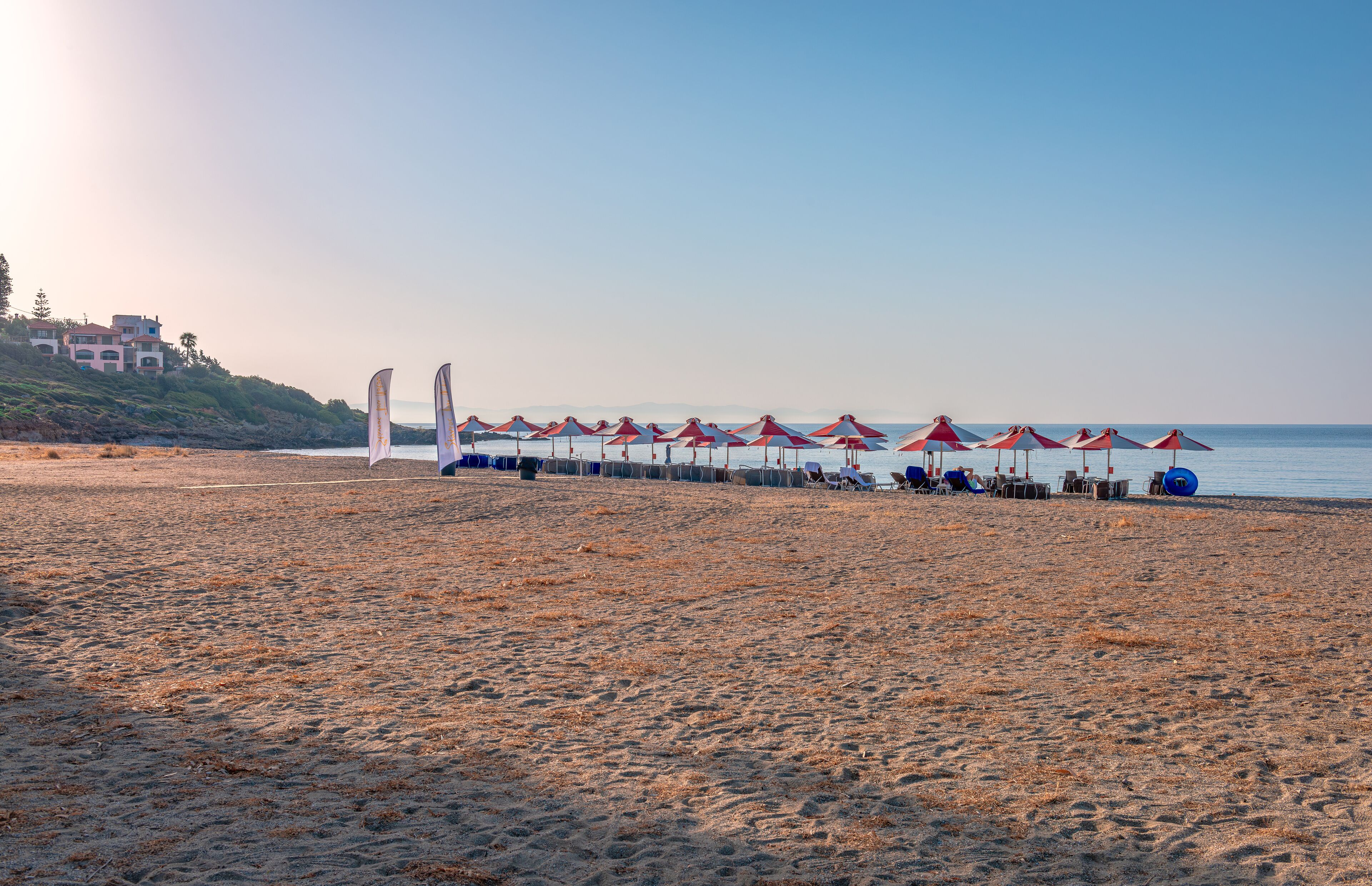 A beach with red and white umbrellas, a row of beach chairs, and a building in the background.