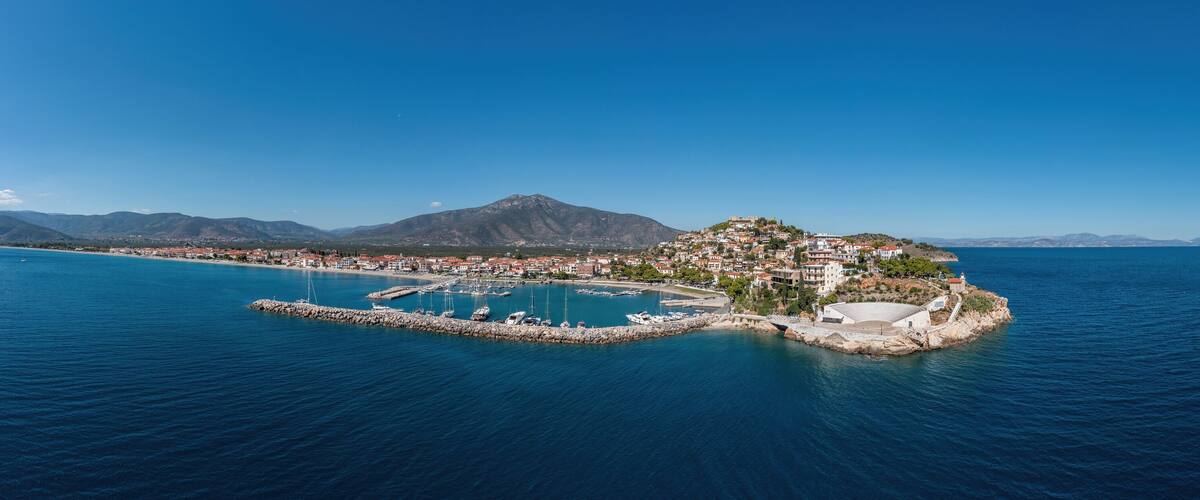 A coastal town with a marina, a small island with buildings, and mountains in the background.