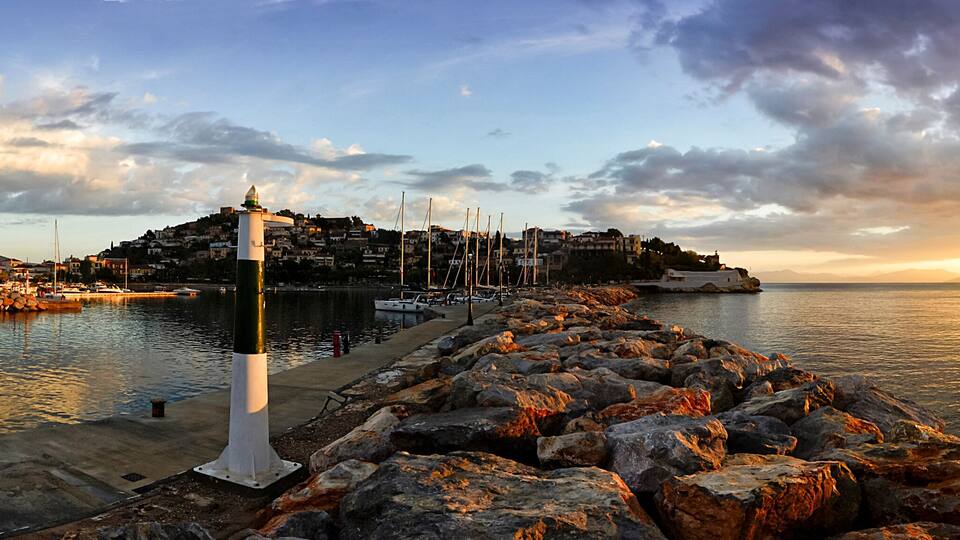 A coastal town with a prominent lighthouse, rocky shoreline, and a mountain in the background.