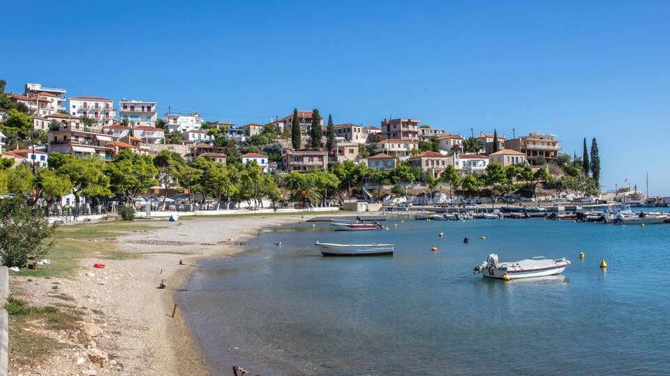 A coastal town with buildings on a hillside, a sandy beach, and boats in the water.