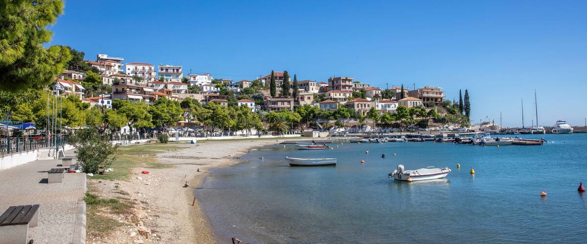 A coastal town with buildings on a hillside, a sandy beach, and boats in the water.