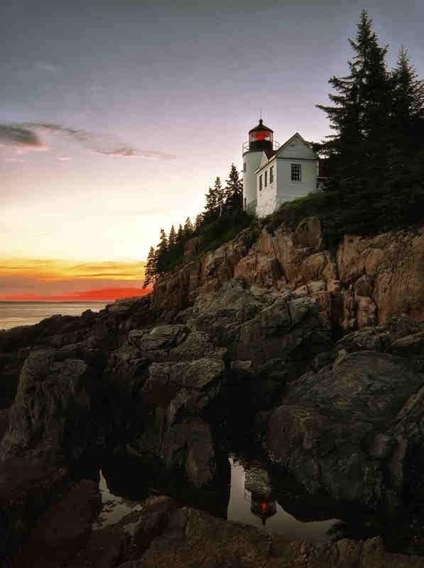 A lighthouse on a rocky cliff with a sunset in the background.