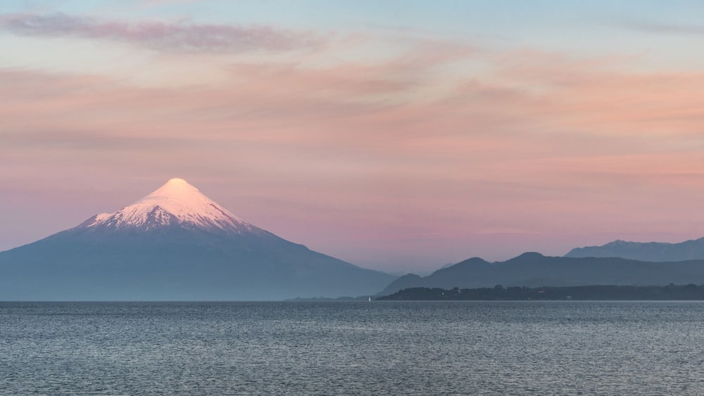 A mountain with a snow-capped peak, a body of water, and a small boat.