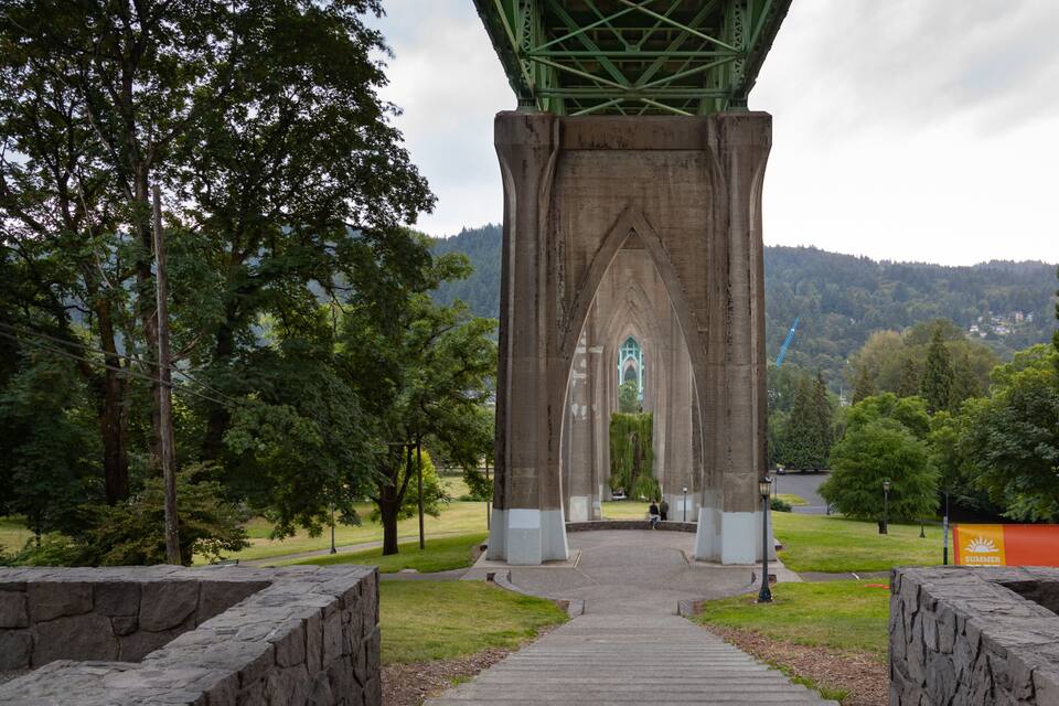 A stone archway leading to a cathedral in a park.