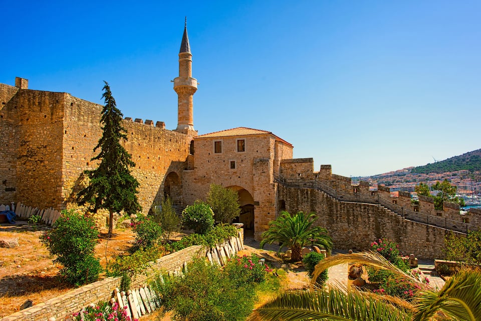 A historic stone fortress with a prominent minaret, lush greenery, and a clear blue sky.