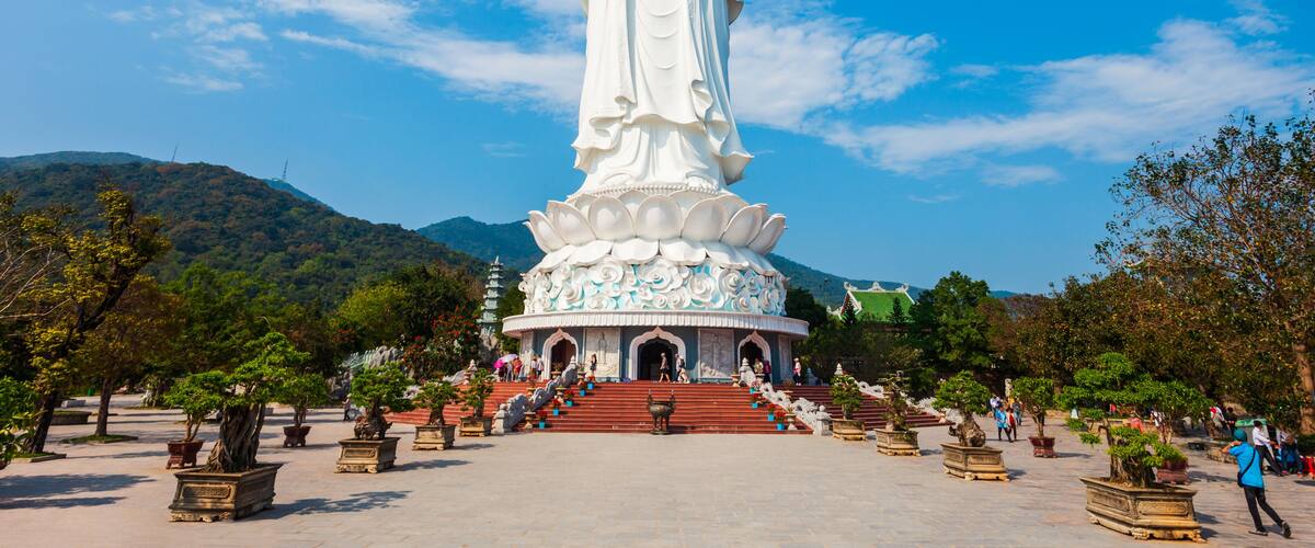 A large white statue with a lotus base, surrounded by potted plants and stairs leading up to it.