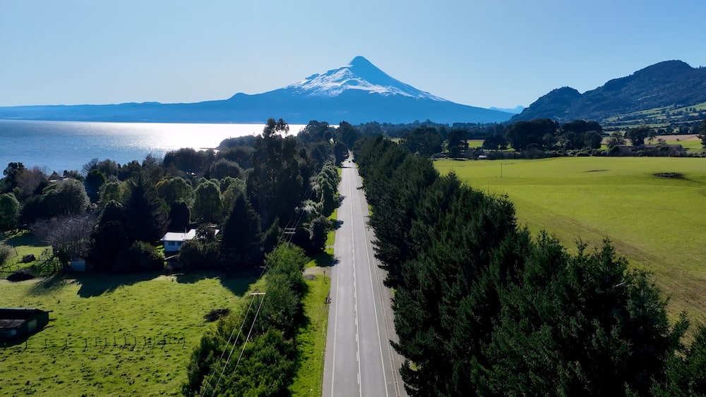 A road leading to a mountain, surrounded by green fields and trees.