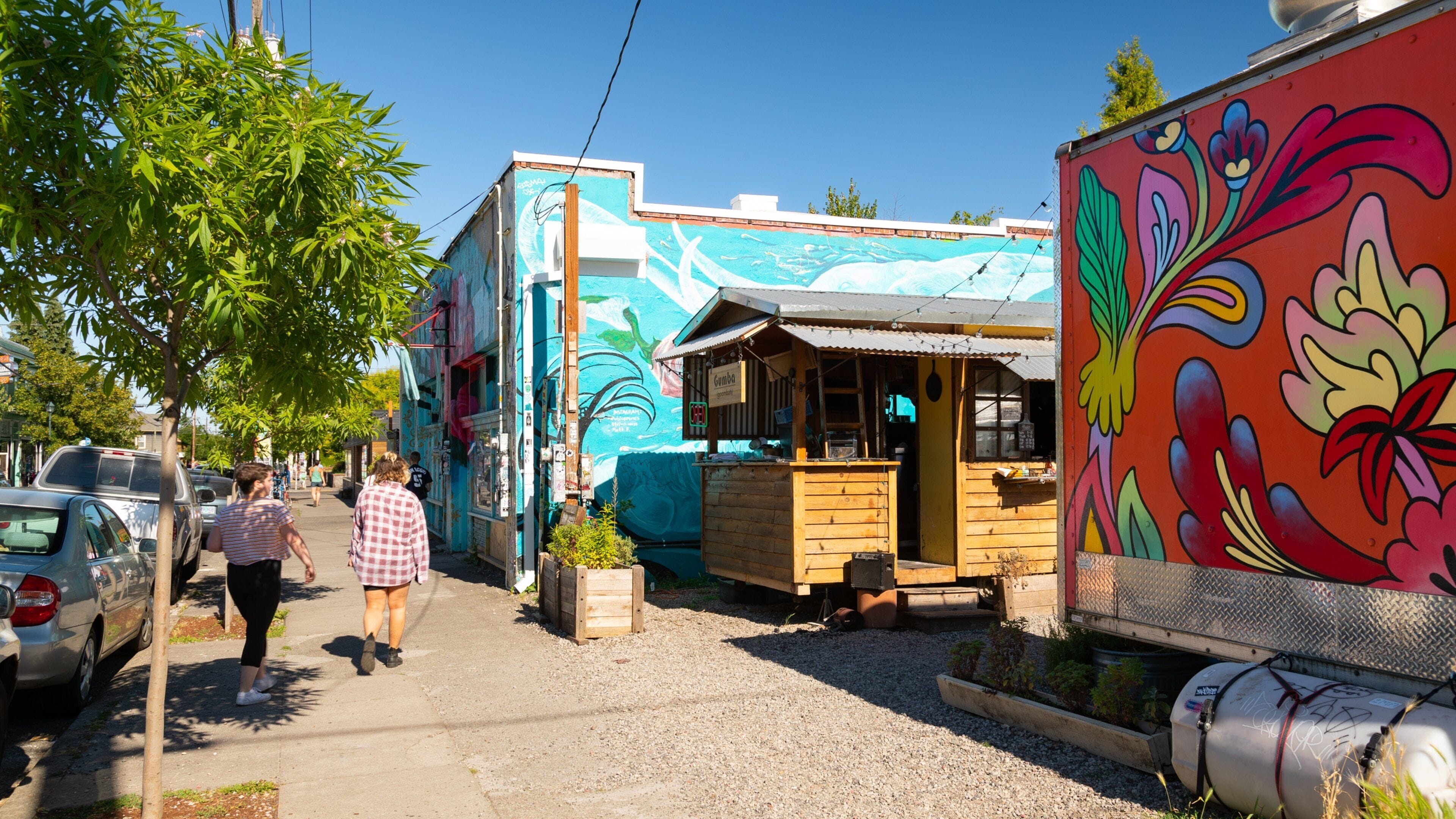 A colorful street with a mural, a wooden structure, and parked cars.