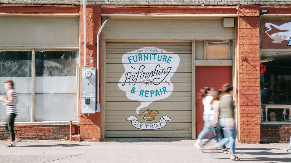 A storefront with a sign that reads "Furniture Refinishing & Repair" and a cartoon character.
