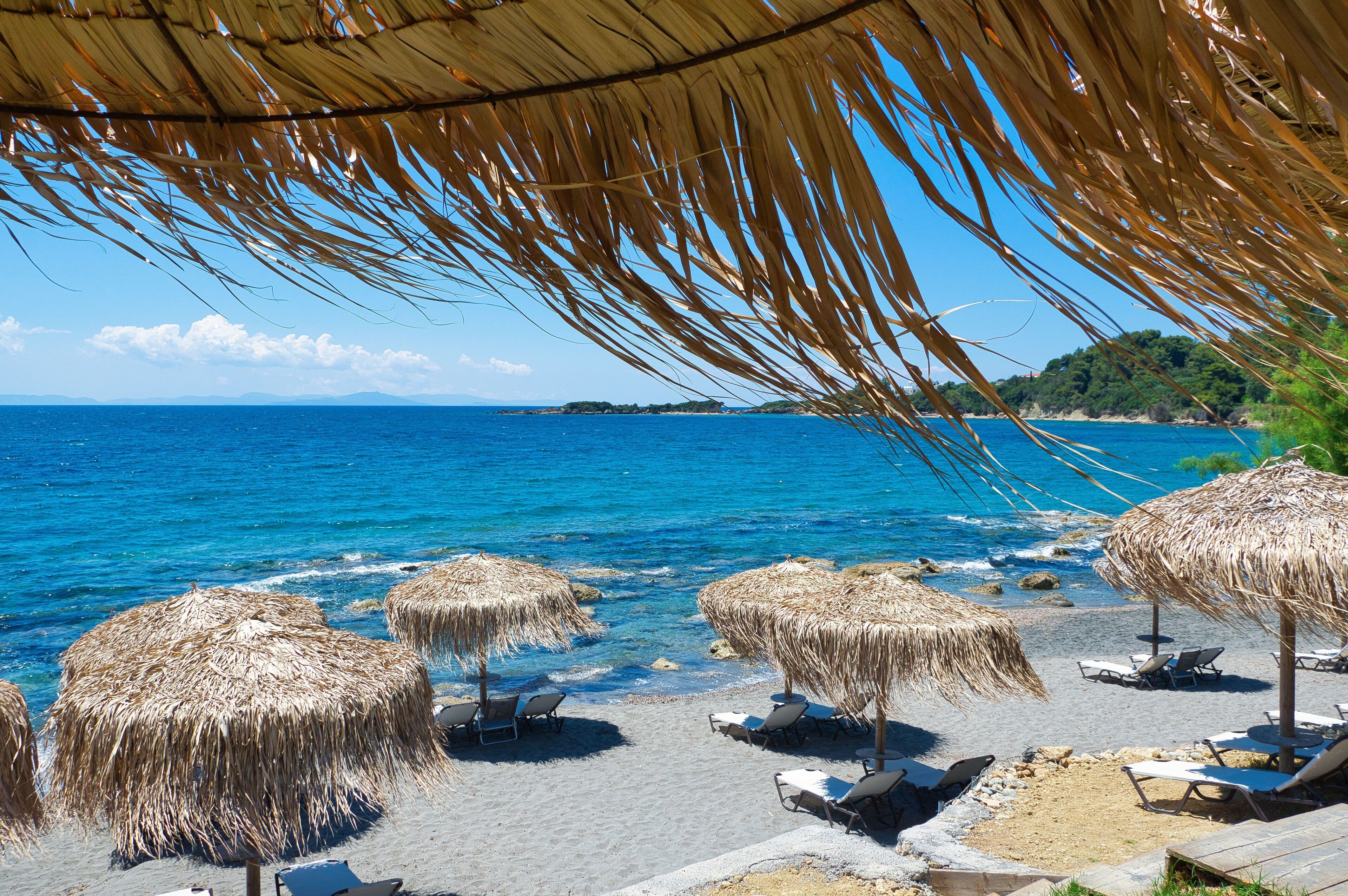 A beach with thatched umbrellas and sun loungers.