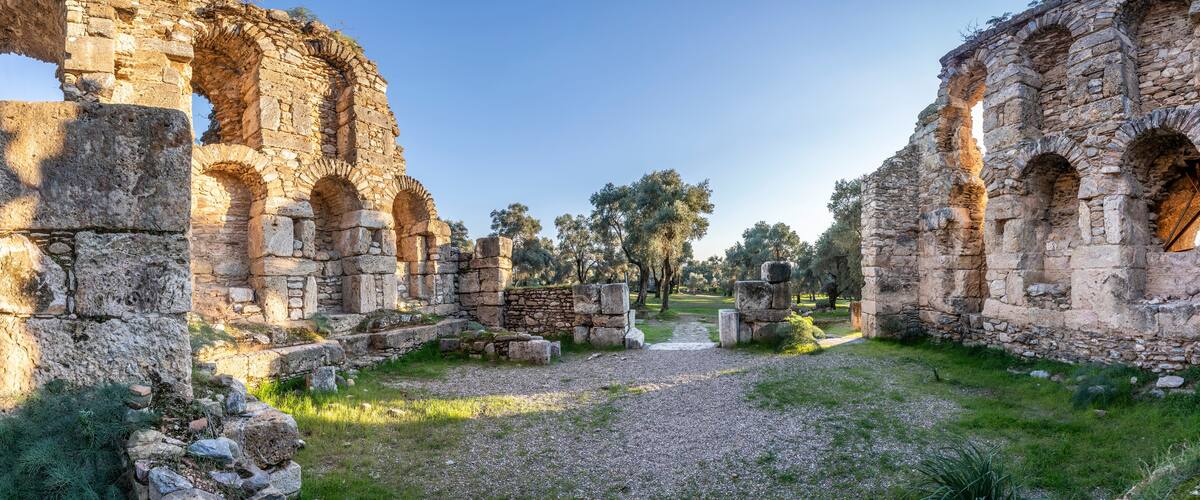 Ancient stone ruins with arches and columns, surrounded by trees and a gravel path.