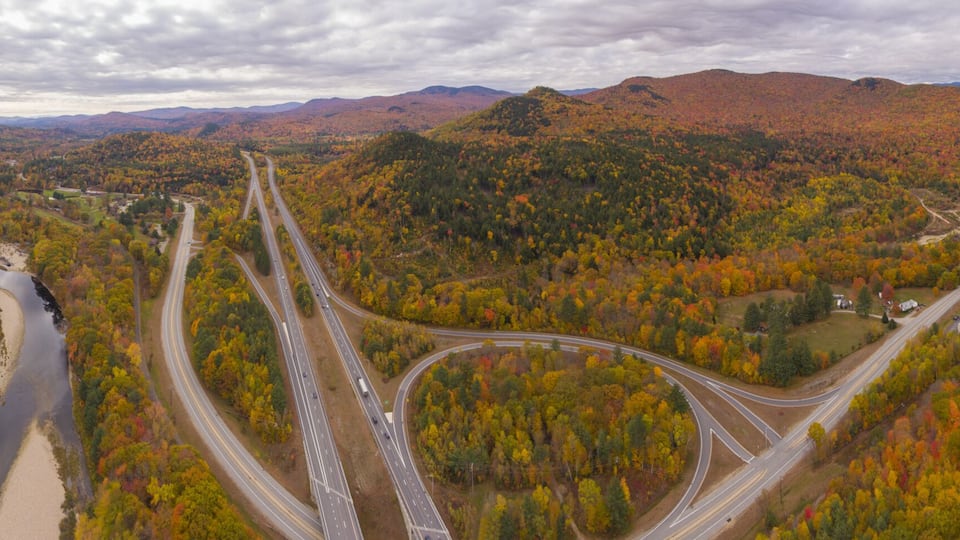 A highway curving through a mountainous area with autumn foliage.