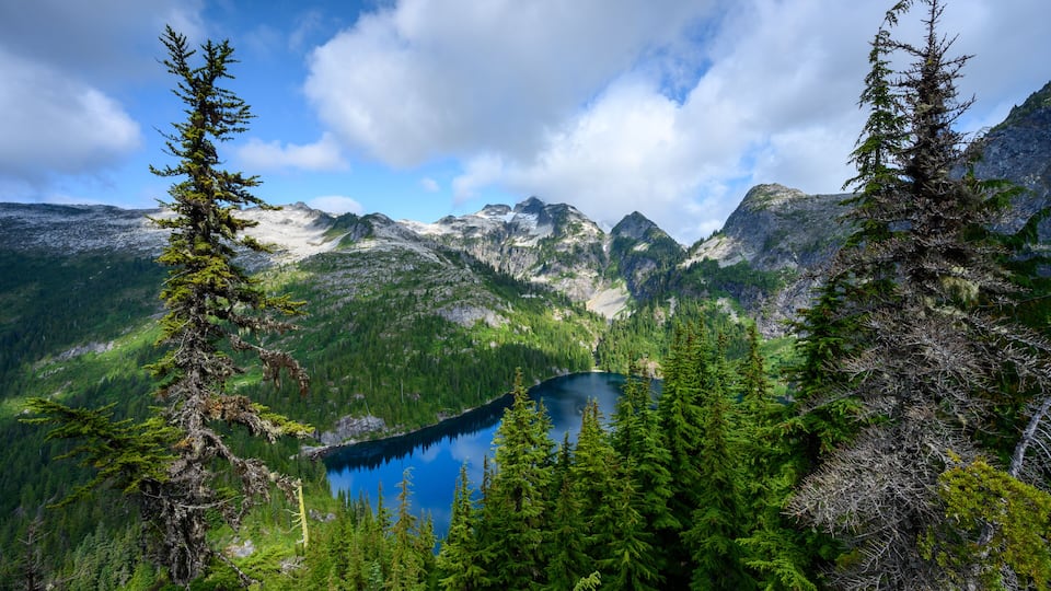 A mountain landscape with a clear blue lake surrounded by dense coniferous forests and rugged peaks.
