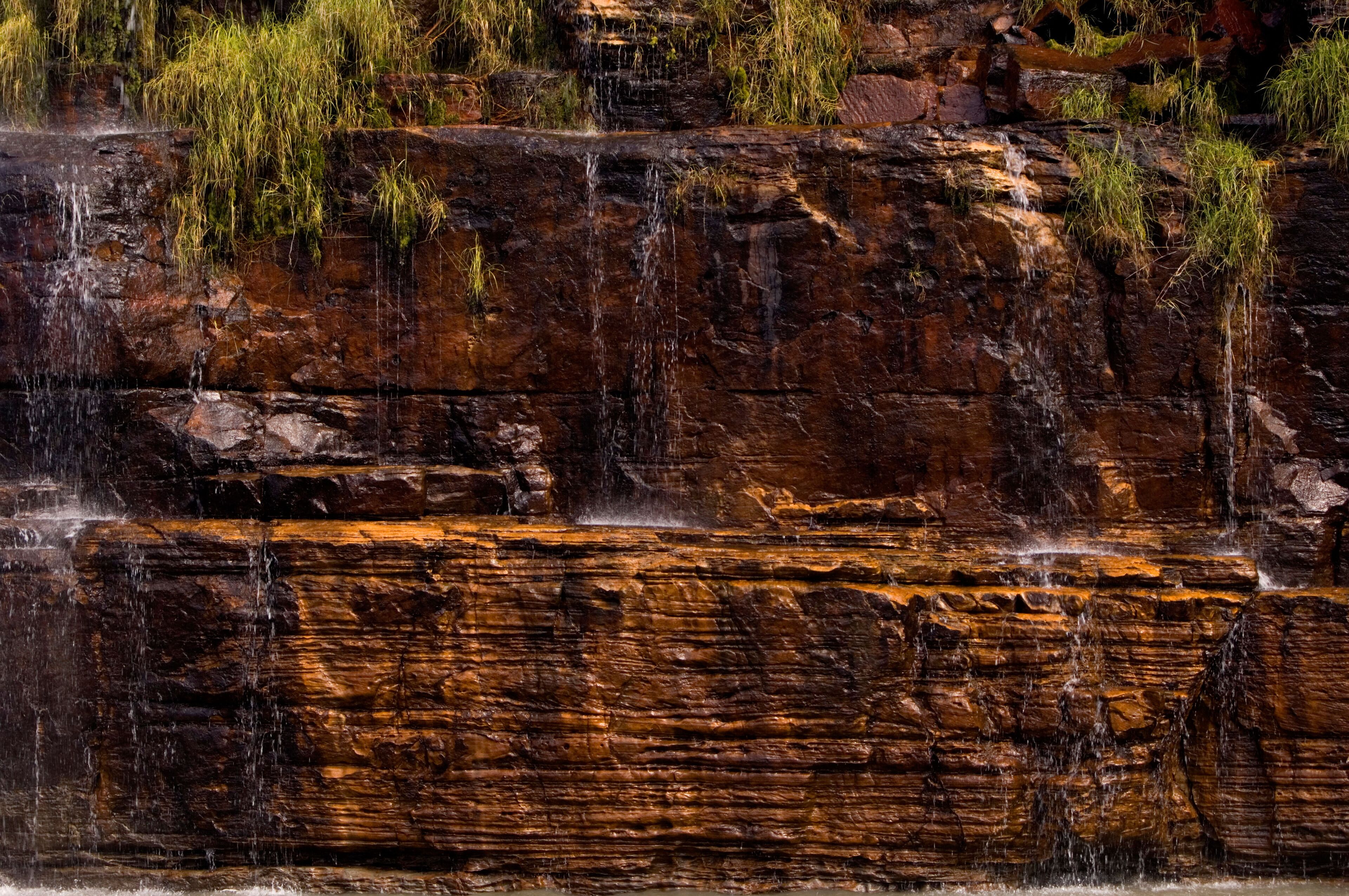 A waterfall cascading over layered rock formations with patches of grass.