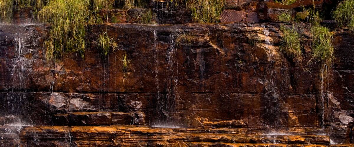 A waterfall cascading over layered rock formations with patches of grass.
