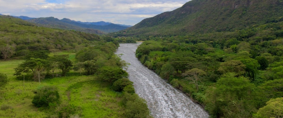 A river winding through a lush valley with dense greenery and hills in the background.
