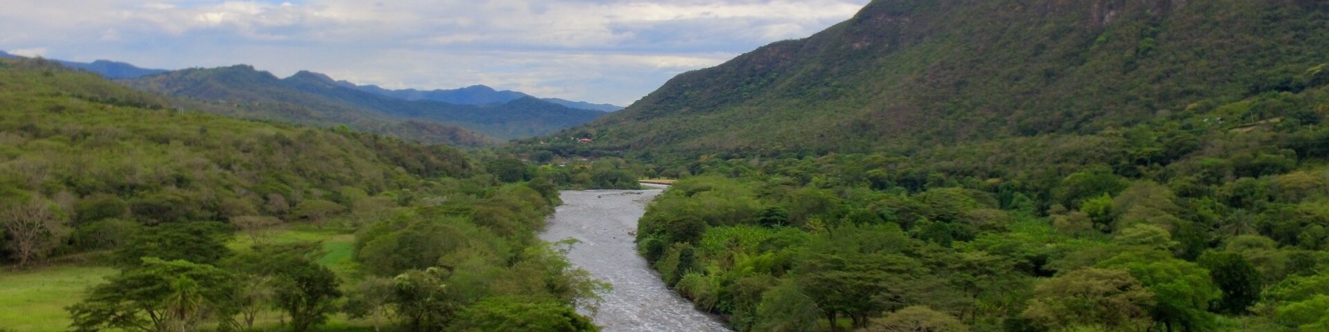 A river winding through a lush valley with dense greenery and hills in the background.