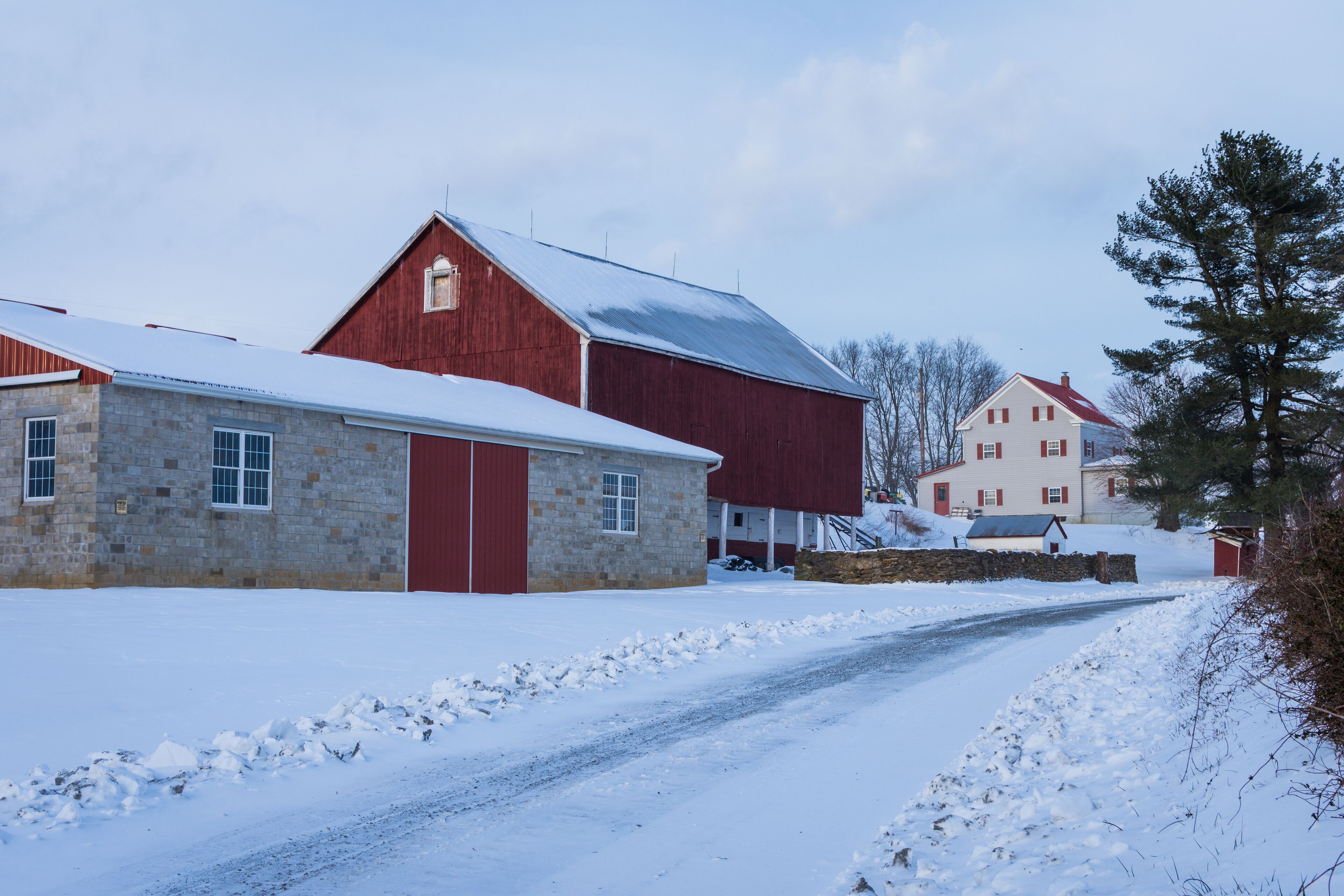 A snow-covered rural road with a stone building and a red barn.