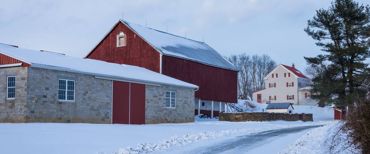 A snow-covered rural road with a stone building and a red barn.