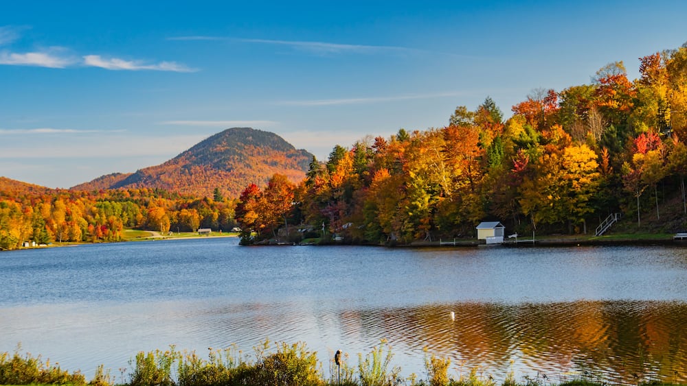 Ein See, umgeben von herbstlich gefärbten Bäumen und einem Berg im Hintergrund.