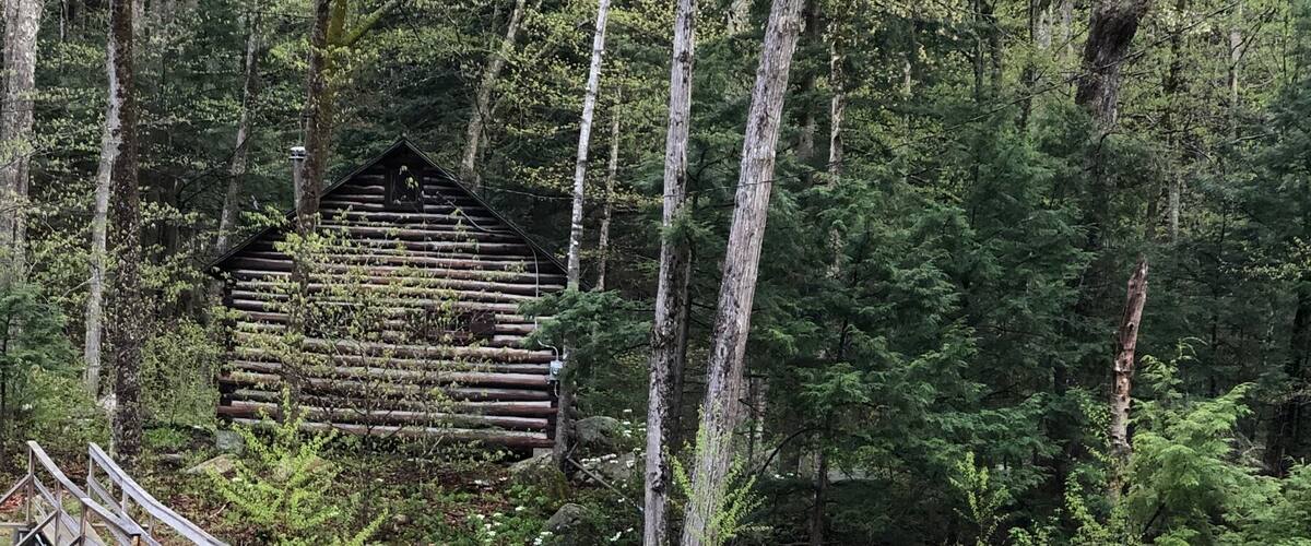 A wooden bridge over a stream with a log cabin in the background.