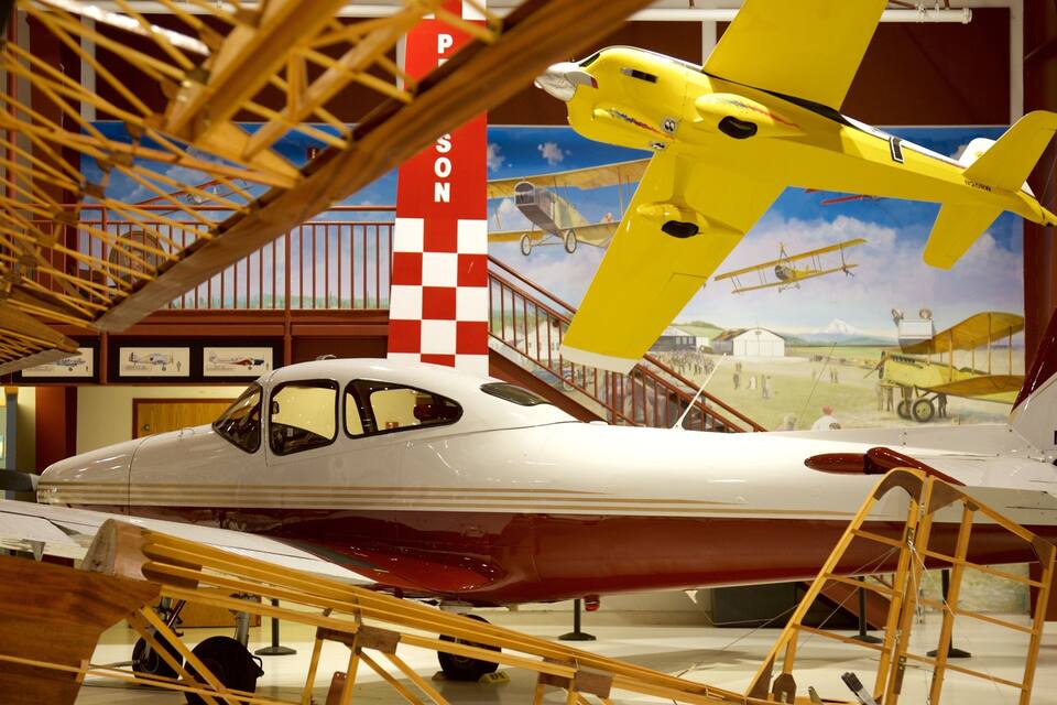 A museum exhibit with a white and red vintage airplane, a yellow biplane, and a red and white checkered flag.