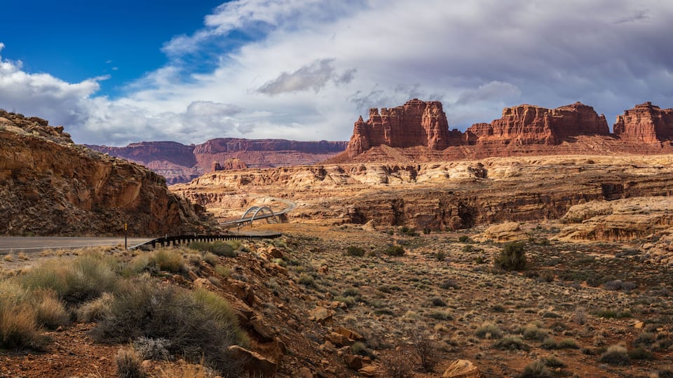 A desert landscape with red rock formations, a road, and sparse vegetation.