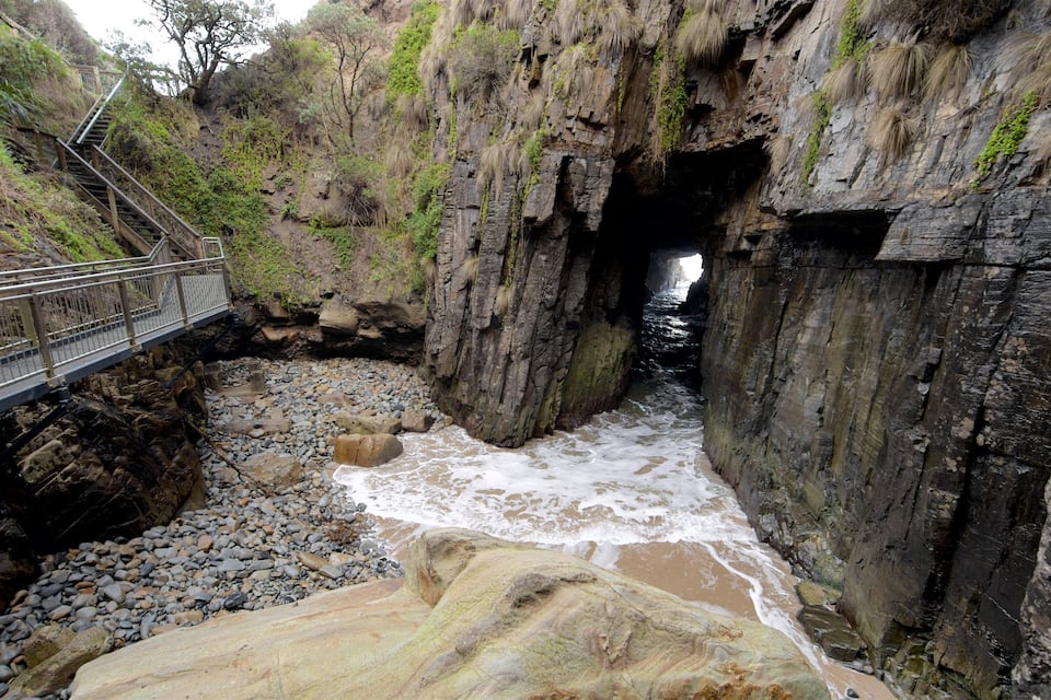 A rocky coastal area with a bridge and a cave entrance.