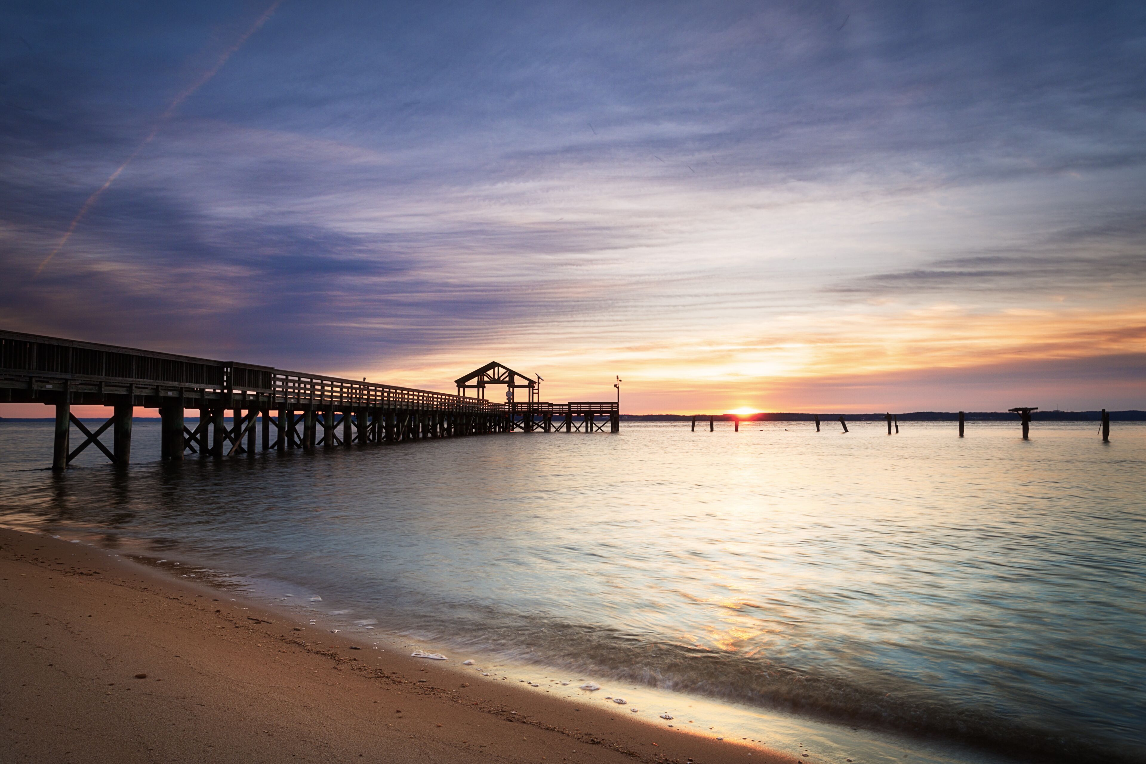 A pier extending into calm waters at sunset with a clear sky.