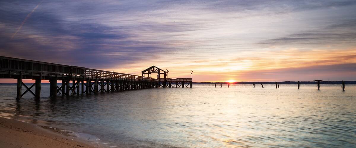 A pier extending into calm waters at sunset with a clear sky.