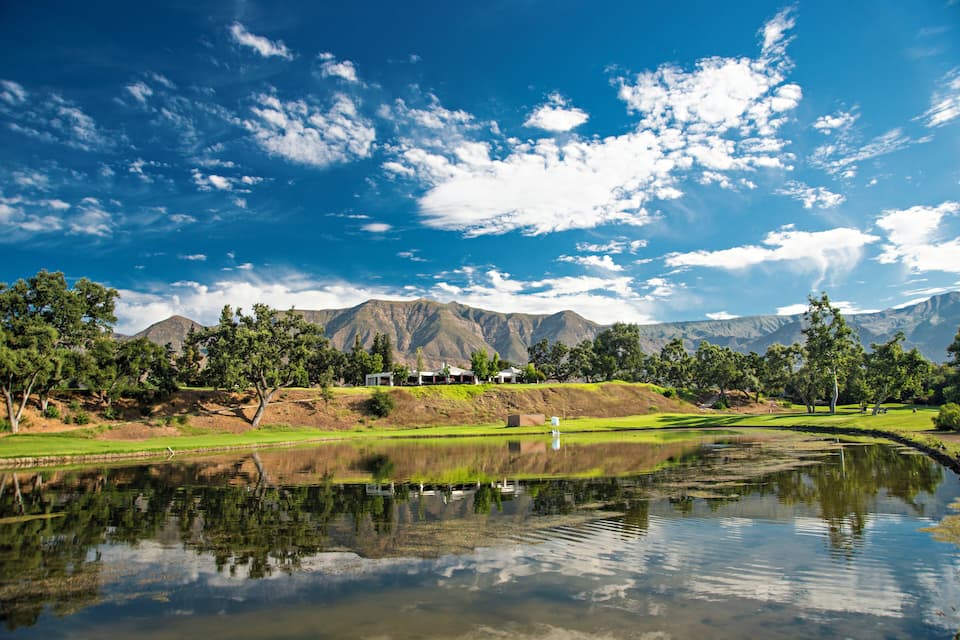 Een meer met weerspiegelingen, bergen en een golfbaan.