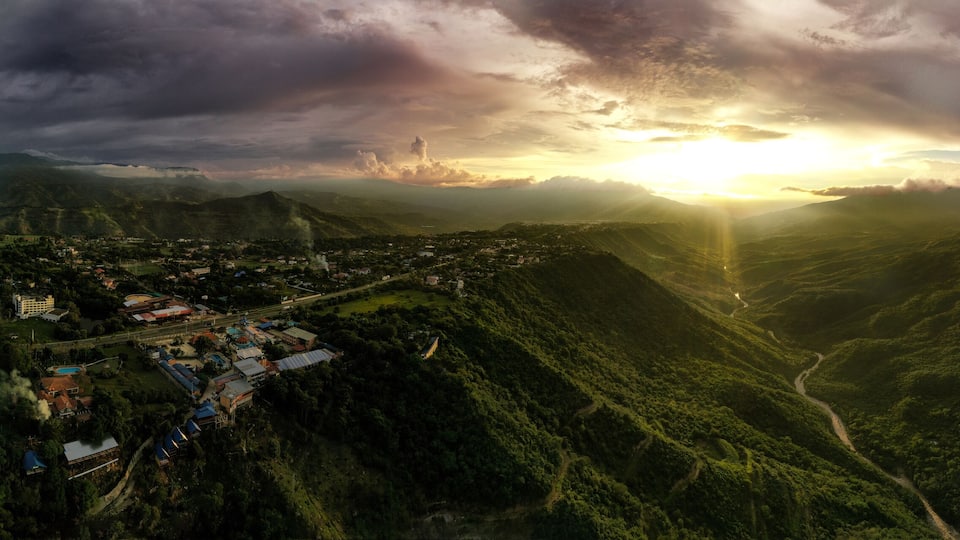 A mountainous landscape with a valley, a town with buildings, and a sunset.