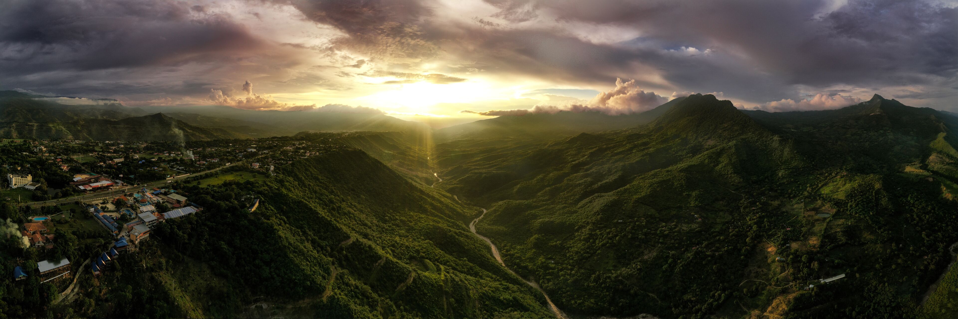 A mountainous landscape with a valley, a town with buildings, and a sunset.
