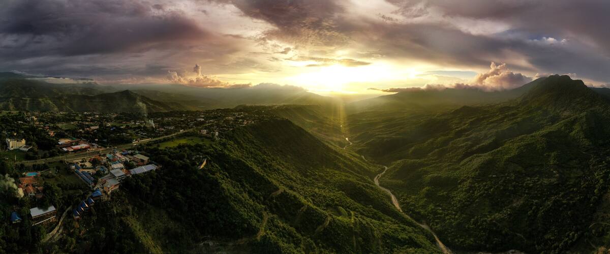 A mountainous landscape with a valley, a town with buildings, and a sunset.