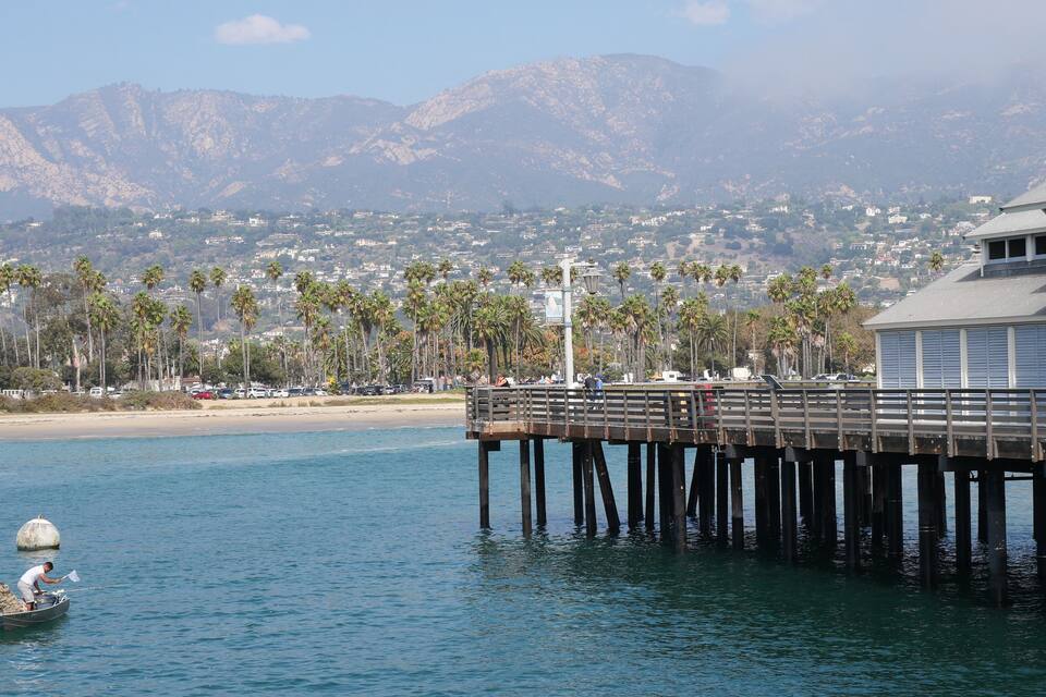 A pier extending into calm waters, palm trees, and a mountainous backdrop.