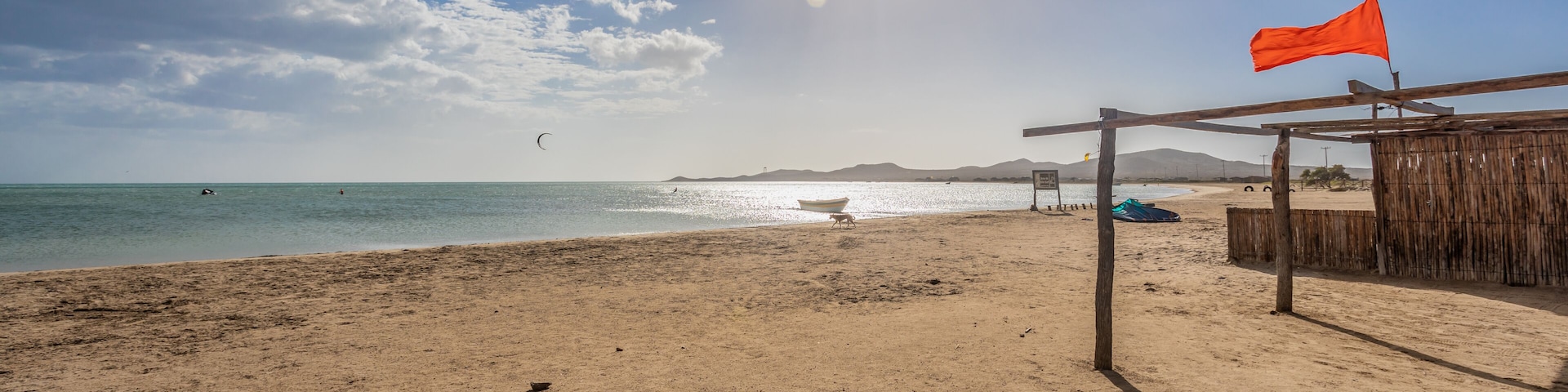 A beach with a wooden structure, a boat, and a flag.